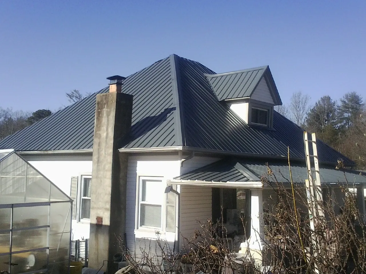 Dark blue standing seam metal roof on a white farmhouse with dormer — Slate & Tile Roof Repair by Roofing Brothers in Diamond