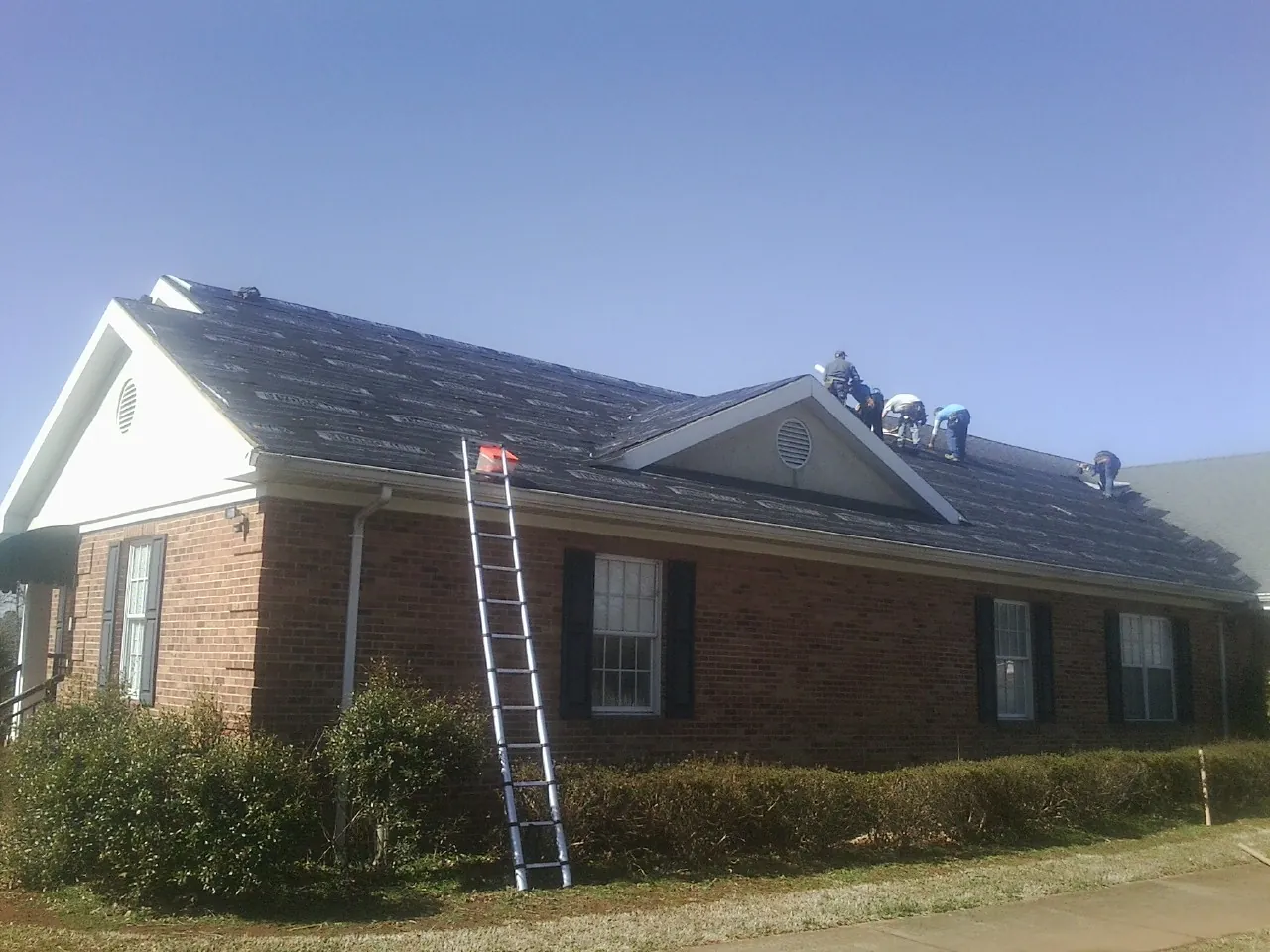 Crew tearing shingles off a brick ranch roof with a ladder set — Emergency Roof Repair work by our crew in Diamond