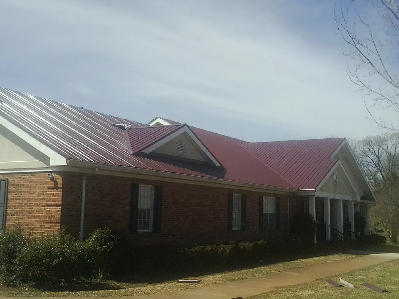 Red metal roof with gabled entries on a long brick building, from a Hail Damage Roof Repair job in Diamond